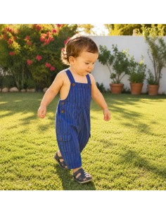 Bebé caminando sobre el césped con peto azul de rayas de Pachamama Kids.