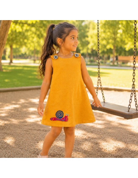 Niña con vestido mostaza Caracol de Pachamama Kids jugando en un parque infantil en un día soleado.